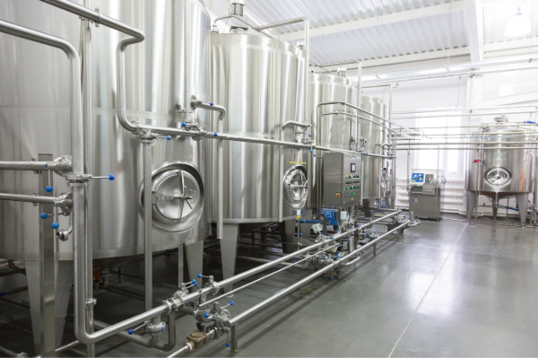 Row of stainless steel storage and process tanks with sanitary piping and control panels inside a bright, clean industrial production hall