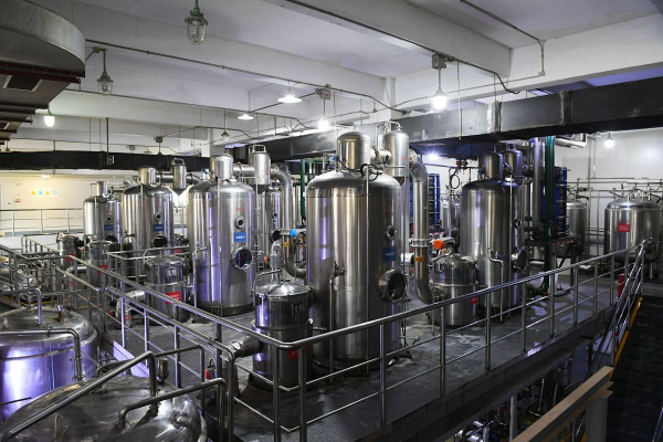 Multiple stainless steel process vessels and columns on an elevated platform with walkways, piping and lighting inside a modern industrial processing facility