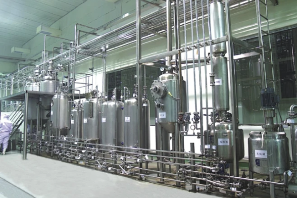 Row of stainless steel process vessels, columns and sanitary piping with an operator working inside a clean industrial purification and distillation workshop
