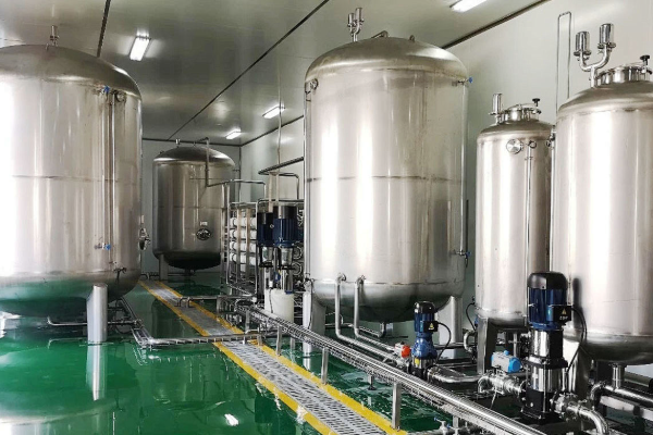 Row of stainless steel storage tanks with pumps and sanitary piping inside a bright, clean industrial process room