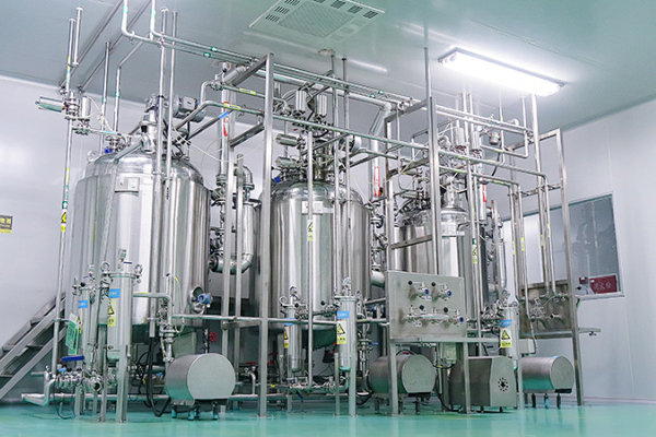 Multiple stainless steel process vessels with sanitary piping, pumps and control valves inside a bright cleanroom industrial production workshop