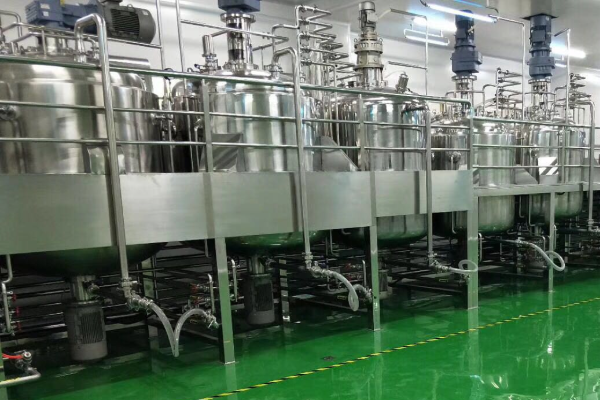 Row of stainless steel mixing and process tanks with agitator motors, platforms and sanitary piping inside a clean industrial production workshop
