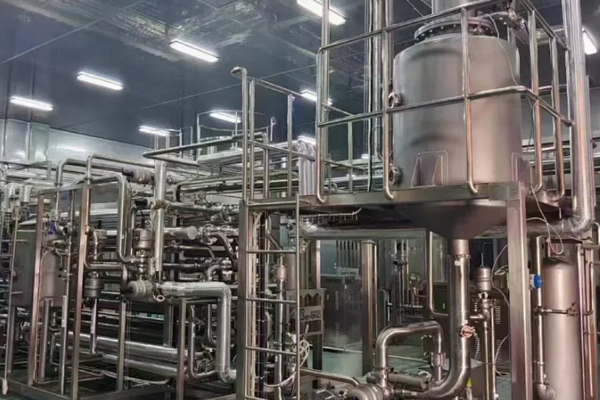 Complex network of stainless steel process vessels, piping and elevated platforms inside a modern industrial processing workshop