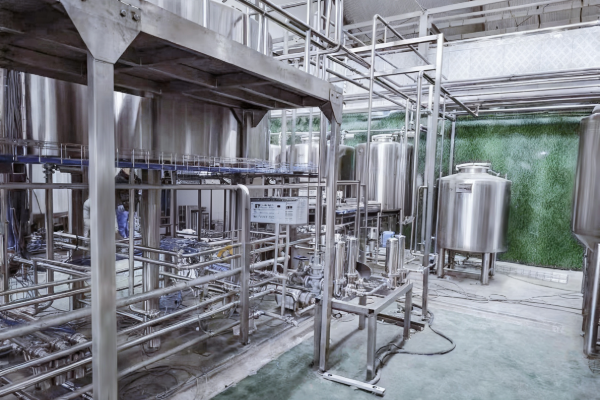 Stainless steel tanks, frames and sanitary piping forming a process system inside a clean industrial production workshop with a green wall background
