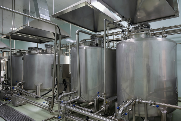 Stainless steel mixing and process tanks with sanitary piping and ventilation hoods inside a clean industrial production room
