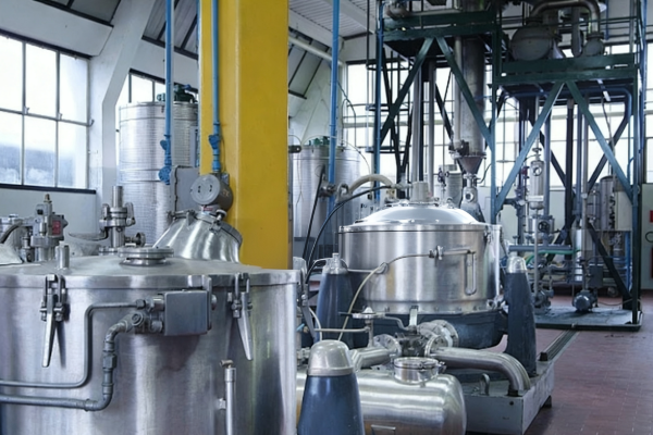 Stainless steel reactor vessels, tanks, pumps and piping inside a modern chemical processing workshop with structural platforms and large windows