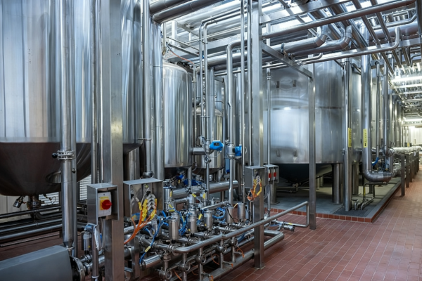 Row of stainless steel process tanks with pumps, valves and overhead piping inside a clean modern industrial production facility