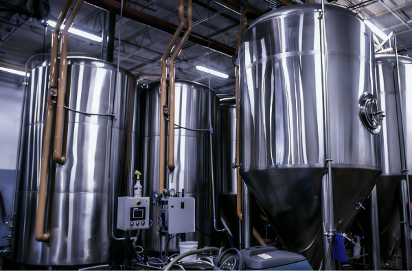 Tall stainless steel process tanks with conical bottoms, control panel and piping inside a modern industrial production facility