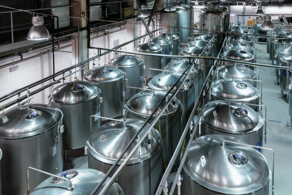 Top view of multiple stainless steel process tanks with piping and overhead walkways inside a clean, modern industrial production facility