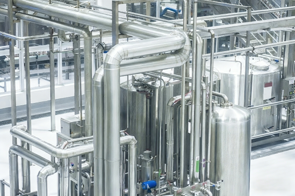 Close-up of stainless steel pipes, tanks and process equipment inside a bright, clean industrial production facility